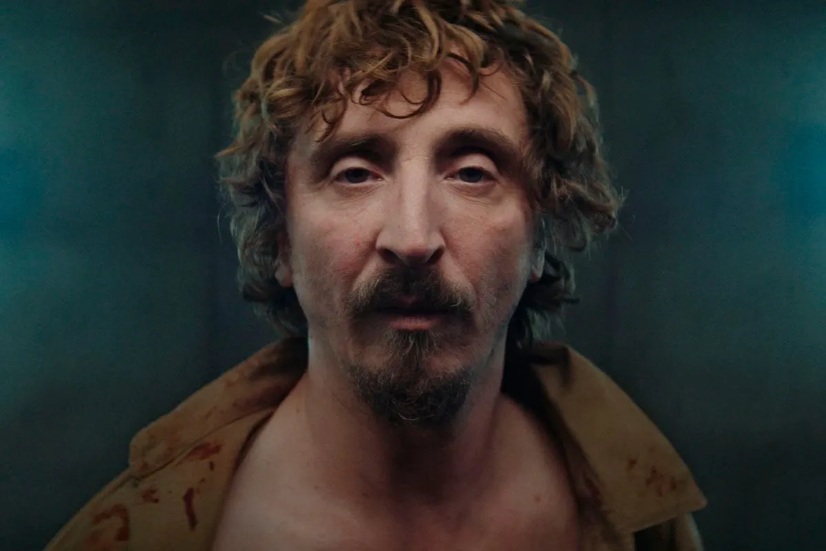 Goreng, con su mirada perdida, reflexiona sobre la explicación detallada del final de la película El Hoyo, mientras la sangre mancha su camisa.