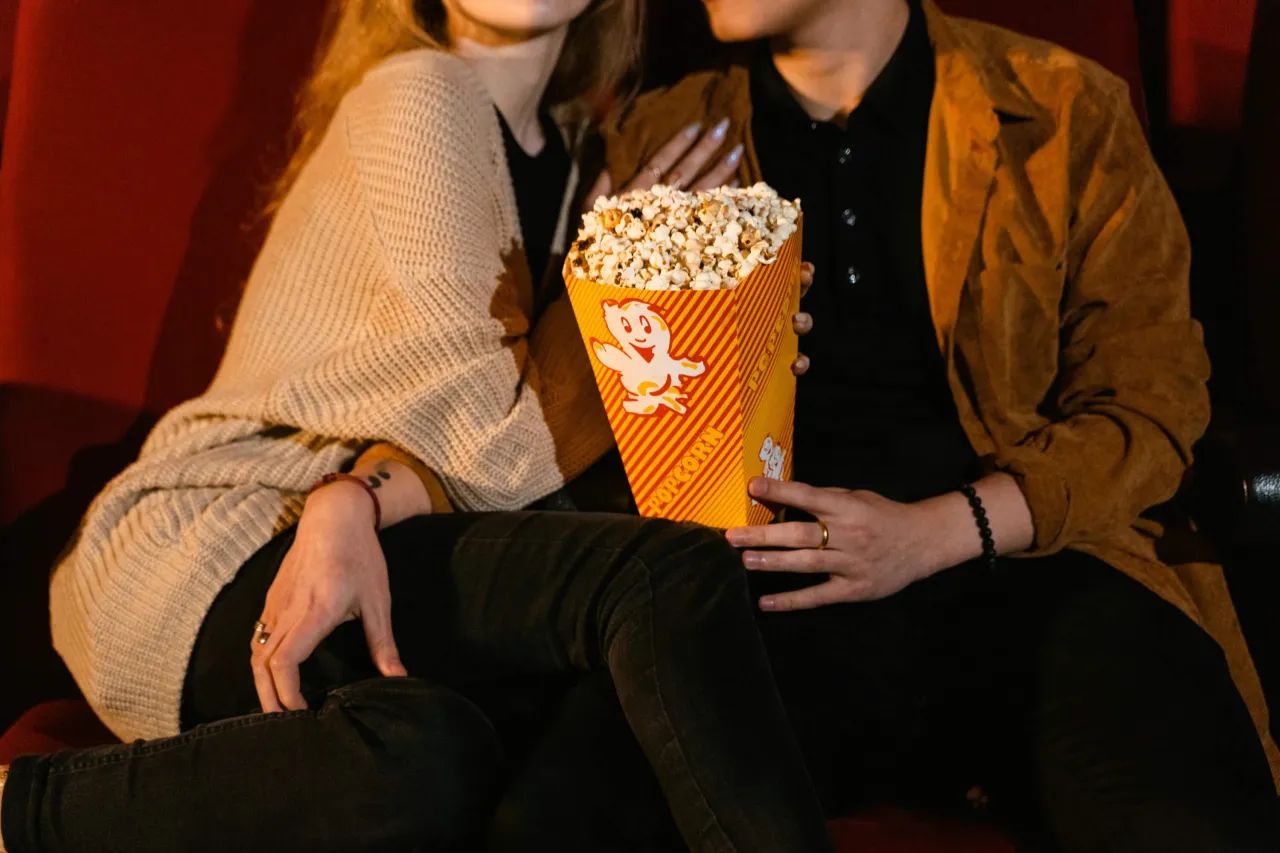 Pareja compartiendo palomitas en el cine, disfrutando de películas con giros de guion imposibles de adivinar.