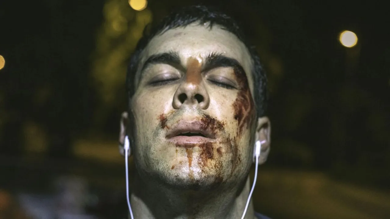 Un hombre con la cara ensangrentada y los ojos cerrados, escuchando música. Ideal para películas de terror psicológico sin jumpscares ni sustos fáciles.